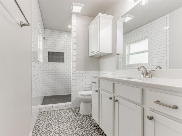 bathroom with a tile shower, vanity, tile walls, and toilet