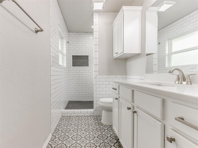 bathroom with a tile shower, vanity, toilet, and tile walls