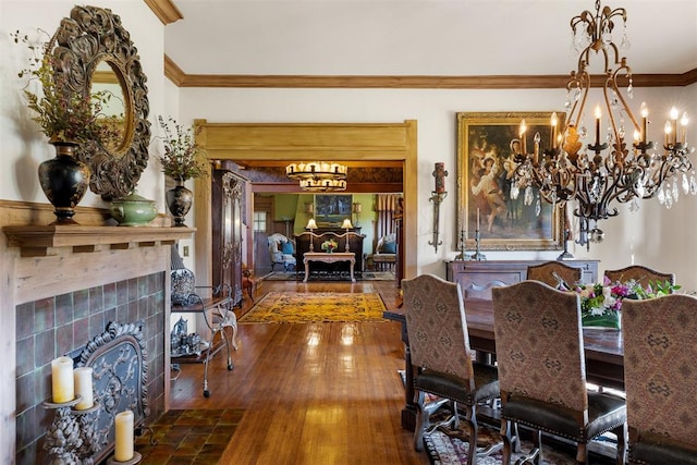 dining room featuring a tiled fireplace, hardwood / wood-style floors, an inviting chandelier, and ornamental molding