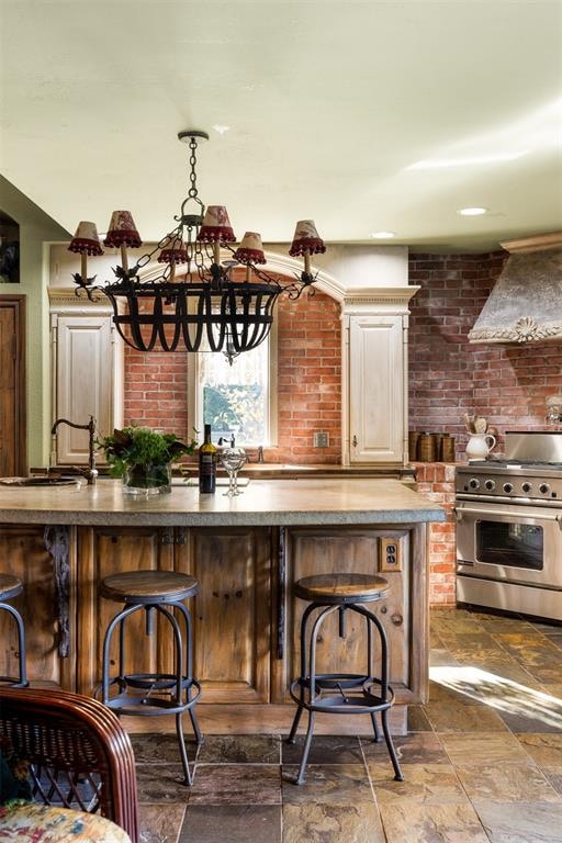 bar with brick wall, stainless steel range, custom exhaust hood, sink, and a chandelier