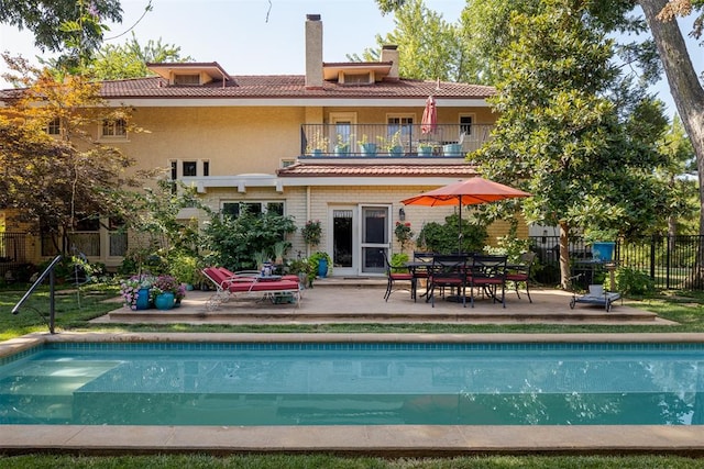 rear view of property with a fenced in pool, a patio area, and a balcony