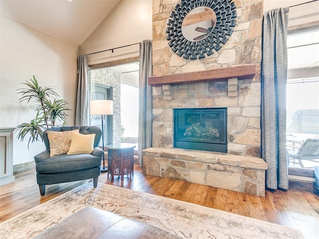 living area with a stone fireplace, wood-type flooring, and vaulted ceiling