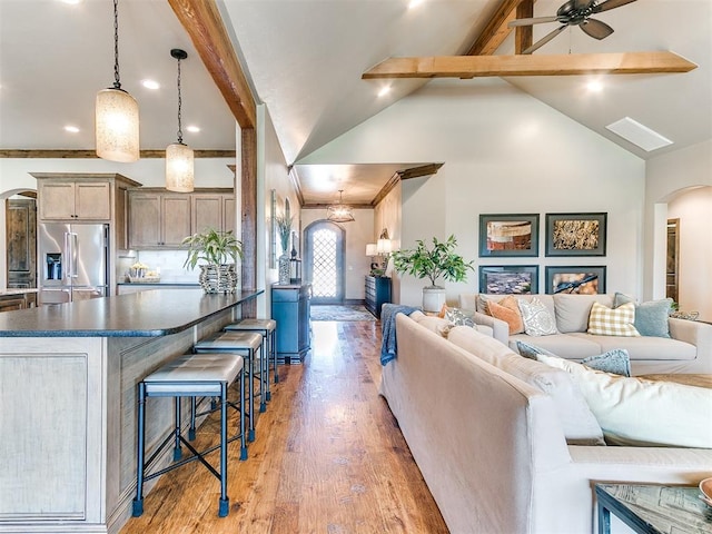 living room featuring light wood-type flooring, ornamental molding, ceiling fan with notable chandelier, high vaulted ceiling, and beamed ceiling