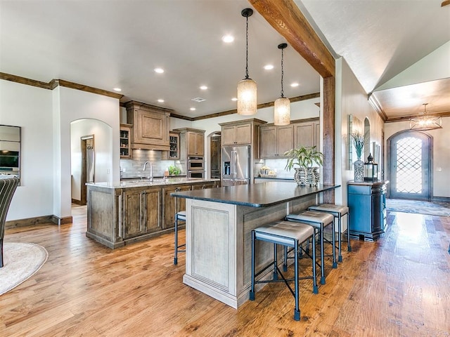 kitchen with a breakfast bar area, pendant lighting, stainless steel appliances, and light hardwood / wood-style flooring