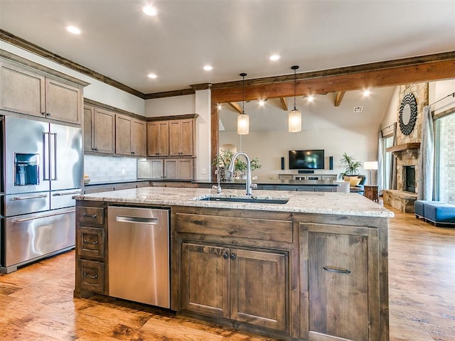 kitchen with hanging light fixtures, sink, light hardwood / wood-style flooring, light stone countertops, and appliances with stainless steel finishes