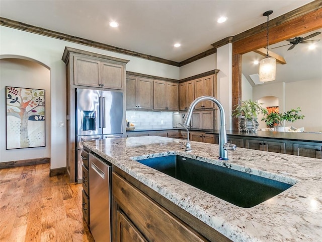 kitchen featuring sink, stainless steel appliances, hanging light fixtures, light stone counters, and light hardwood / wood-style floors