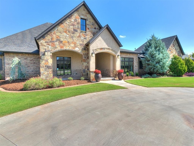 view of front of house featuring a front lawn, roof with shingles, and stone siding