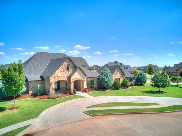 french country style house with curved driveway, a front lawn, and stone siding