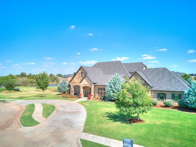 view of front facade featuring curved driveway, a front yard, and stone siding