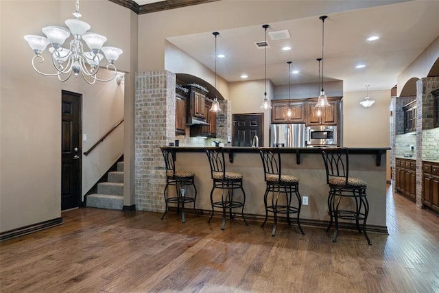 kitchen with stainless steel appliances, dark hardwood / wood-style floors, kitchen peninsula, a chandelier, and a breakfast bar