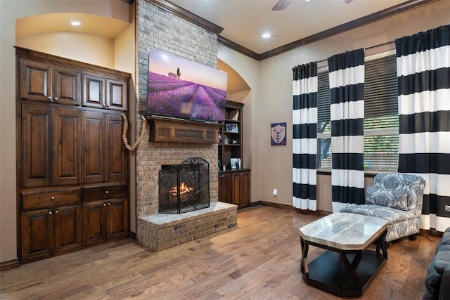 living room with ceiling fan, light hardwood / wood-style flooring, ornamental molding, and a brick fireplace