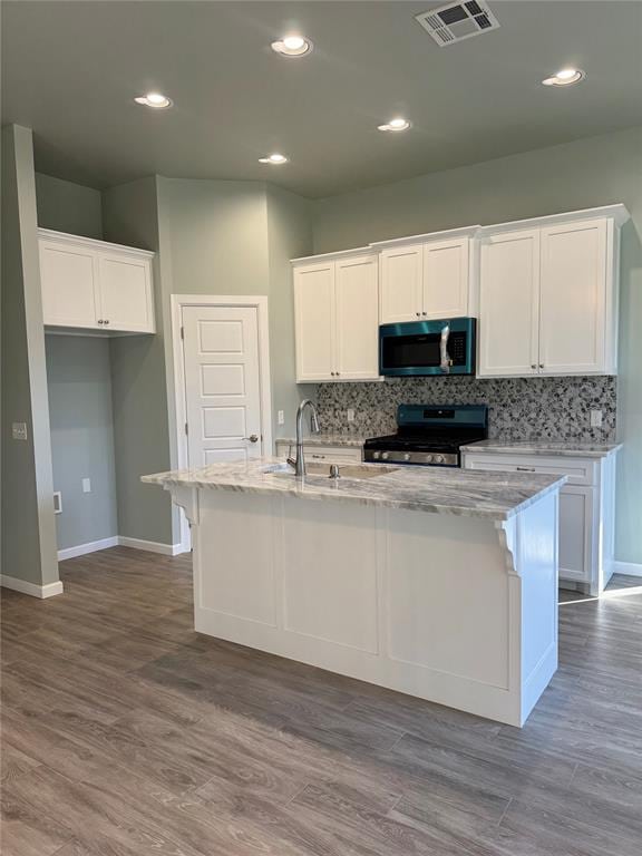 kitchen with appliances with stainless steel finishes, a center island with sink, white cabinetry, and hardwood / wood-style flooring