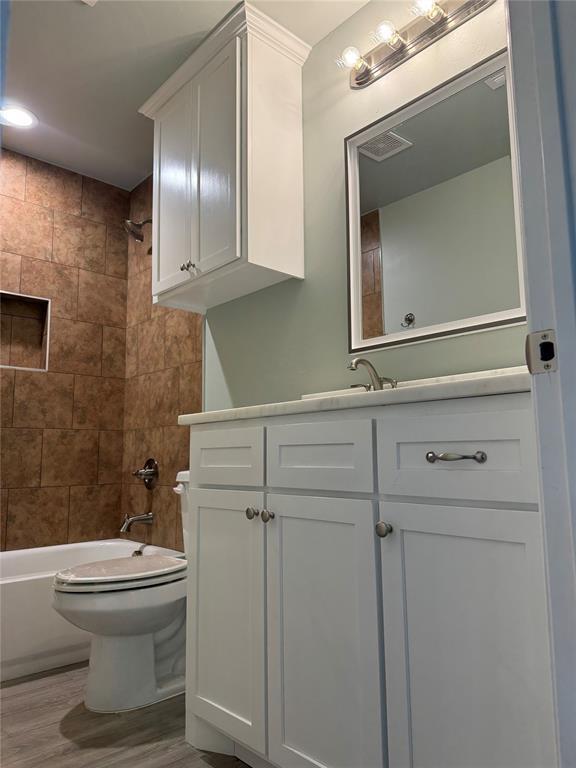 full bathroom featuring vanity, tiled shower / bath combo, wood-type flooring, and toilet