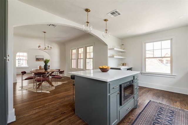 kitchen with stainless steel microwave, hanging light fixtures, an inviting chandelier, dark hardwood / wood-style floors, and a kitchen island