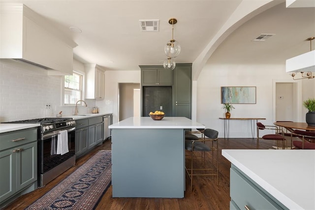 kitchen with backsplash, stainless steel gas range oven, dark wood-type flooring, sink, and pendant lighting