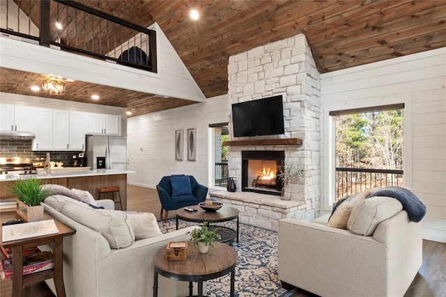 living room with wooden ceiling, high vaulted ceiling, a stone fireplace, wooden walls, and dark hardwood / wood-style flooring