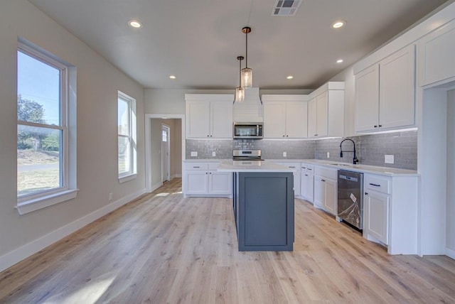 kitchen with light hardwood / wood-style floors, white cabinetry, hanging light fixtures, and appliances with stainless steel finishes