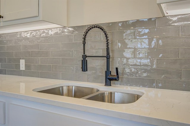 interior details featuring white cabinets, light stone countertops, and sink