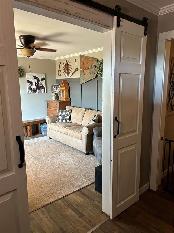 living room featuring ceiling fan, a barn door, dark hardwood / wood-style flooring, and crown molding