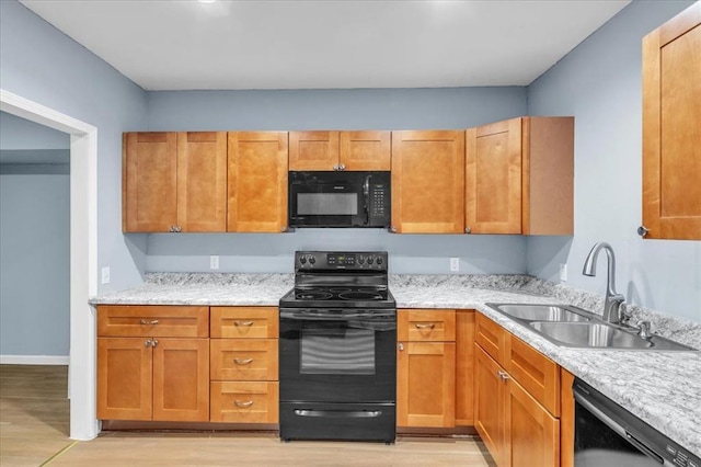 kitchen featuring black appliances, light stone counters, light wood-type flooring, and sink