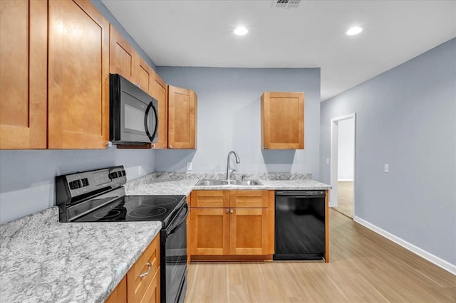 kitchen with light stone counters, sink, black appliances, and light hardwood / wood-style floors