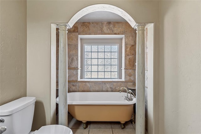 bathroom featuring toilet, tile patterned flooring, ornate columns, and a bathing tub