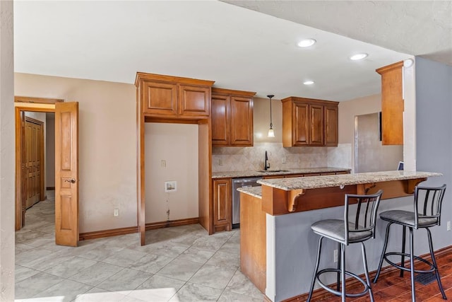 kitchen with pendant lighting, backsplash, stainless steel dishwasher, light stone counters, and kitchen peninsula