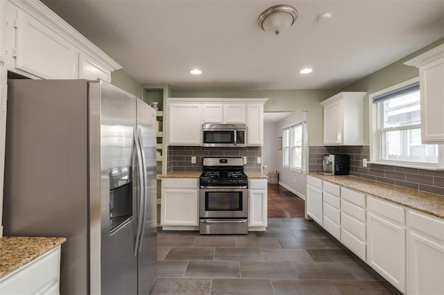 kitchen with tasteful backsplash, light stone counters, stainless steel appliances, dark hardwood / wood-style floors, and white cabinetry