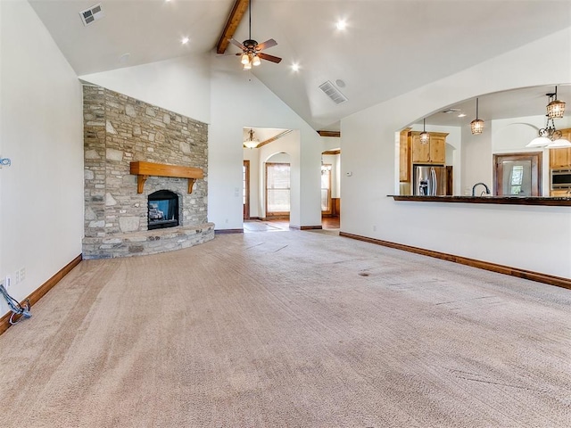 unfurnished living room with high vaulted ceiling, a stone fireplace, ceiling fan, beamed ceiling, and light colored carpet