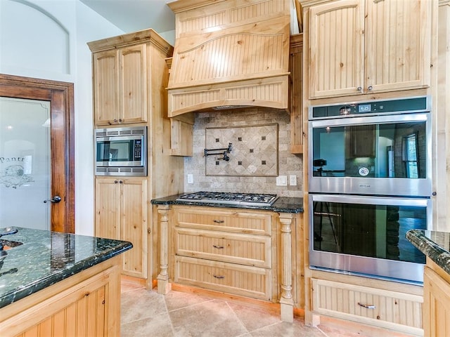 kitchen featuring stainless steel appliances, tasteful backsplash, dark stone countertops, light brown cabinetry, and light tile patterned flooring