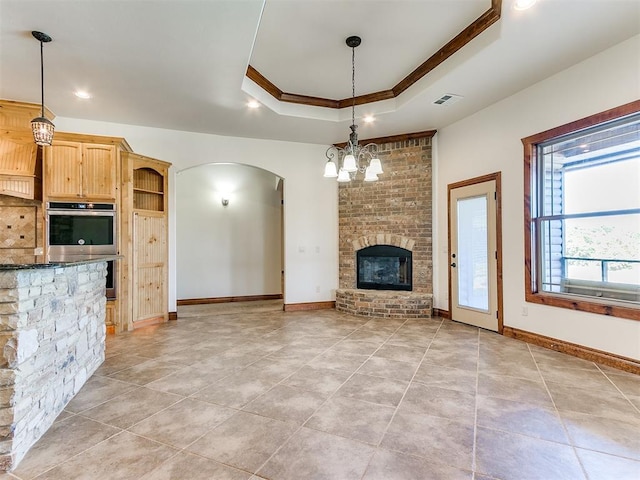 unfurnished living room with crown molding, light tile patterned floors, a fireplace, a tray ceiling, and a chandelier