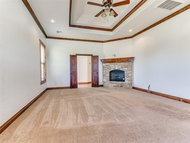 unfurnished living room with a raised ceiling, crown molding, carpet flooring, ceiling fan, and a fireplace