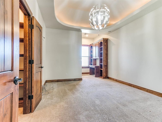 empty room featuring a chandelier, light colored carpet, and a tray ceiling