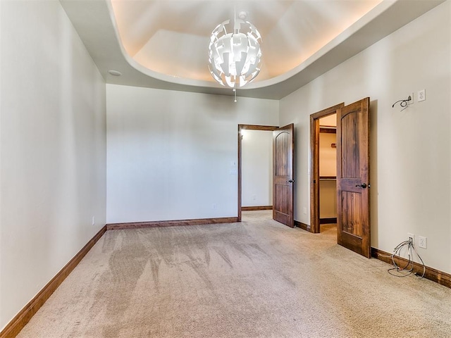 unfurnished room featuring a notable chandelier, light colored carpet, and a tray ceiling