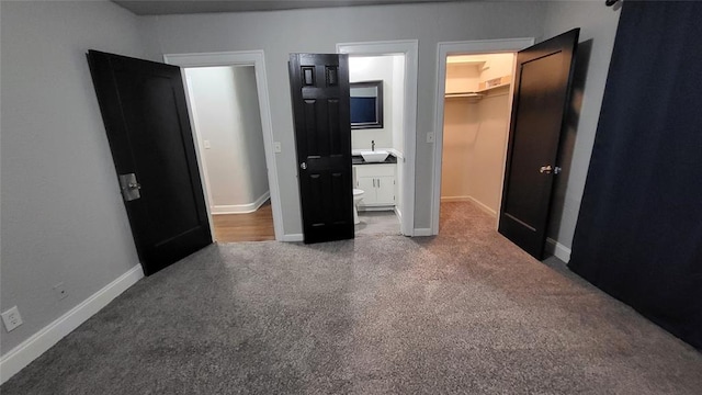 unfurnished bedroom with ensuite bathroom, a walk in closet, sink, carpet floors, and a closet