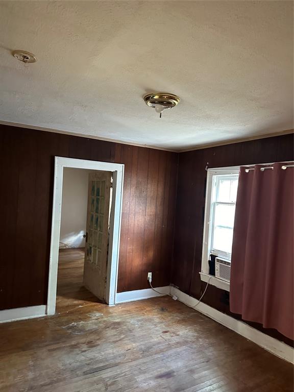 spare room with wooden walls, hardwood / wood-style floors, cooling unit, and a textured ceiling