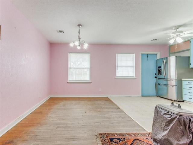 unfurnished dining area with light wood-type flooring, visible vents, a textured ceiling, and baseboards