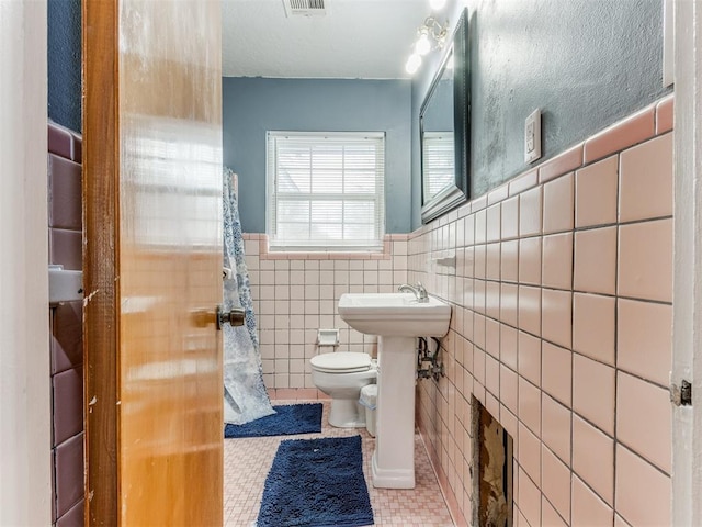 bathroom featuring visible vents, toilet, a wainscoted wall, tile patterned floors, and tile walls