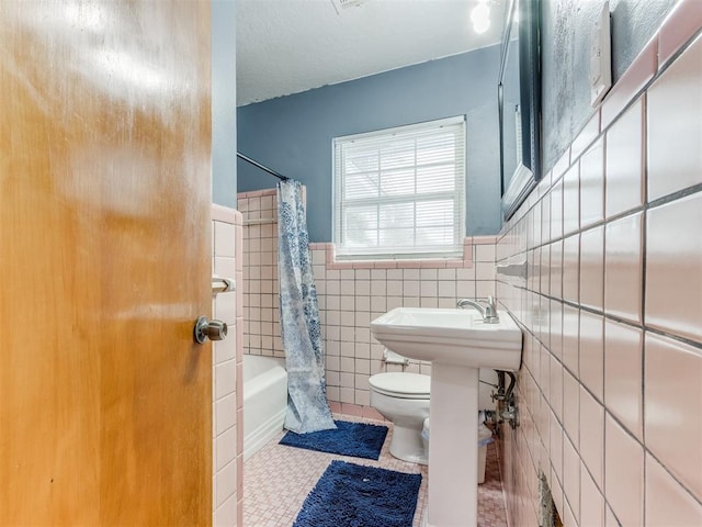 full bathroom featuring shower / tub combo, wainscoting, toilet, tile patterned flooring, and tile walls