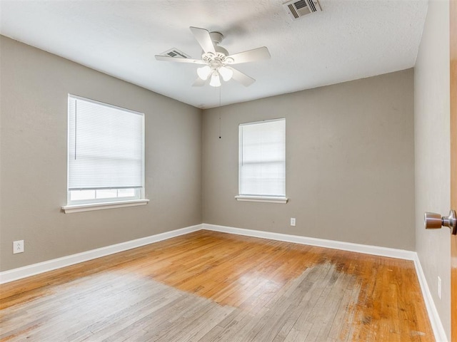 unfurnished room featuring ceiling fan, wood finished floors, visible vents, and baseboards