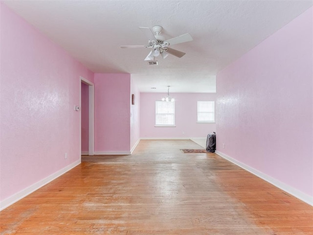 unfurnished room featuring light wood-type flooring, baseboards, visible vents, and ceiling fan with notable chandelier