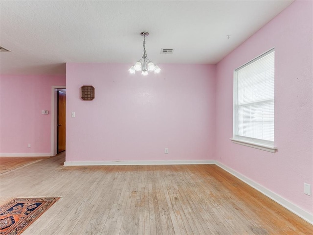 spare room with light wood-type flooring, visible vents, baseboards, and an inviting chandelier