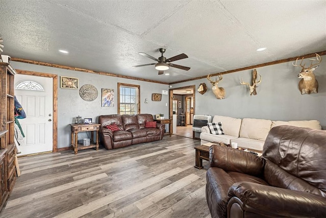 living room with ceiling fan, wood-type flooring, a textured ceiling, and ornamental molding