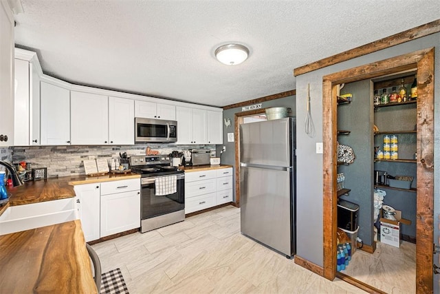 kitchen featuring white cabinetry, sink, stainless steel appliances, tasteful backsplash, and butcher block countertops