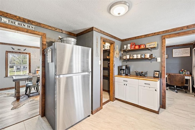 kitchen with stainless steel refrigerator, white cabinetry, wooden counters, crown molding, and a textured ceiling