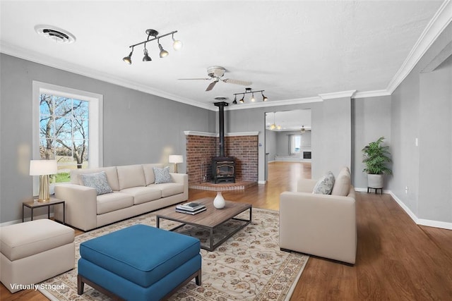 living room with a wood stove, crown molding, ceiling fan, and wood-type flooring