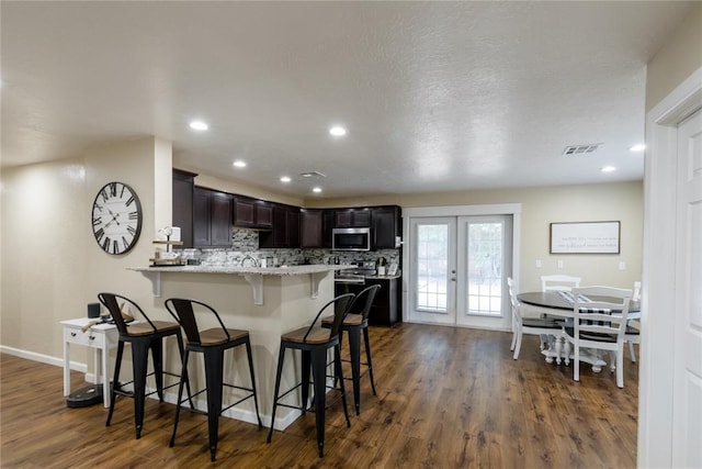 kitchen featuring dark brown cabinetry, stainless steel appliances, dark hardwood / wood-style flooring, a kitchen bar, and decorative backsplash