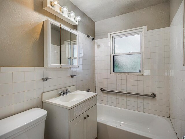 full bathroom featuring tiled shower / bath, vanity, toilet, and tile walls