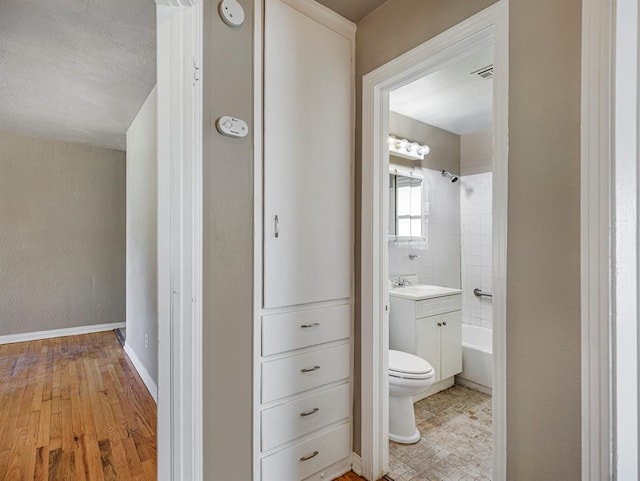 full bathroom with vanity, tiled shower / bath combo, a textured ceiling, hardwood / wood-style floors, and toilet