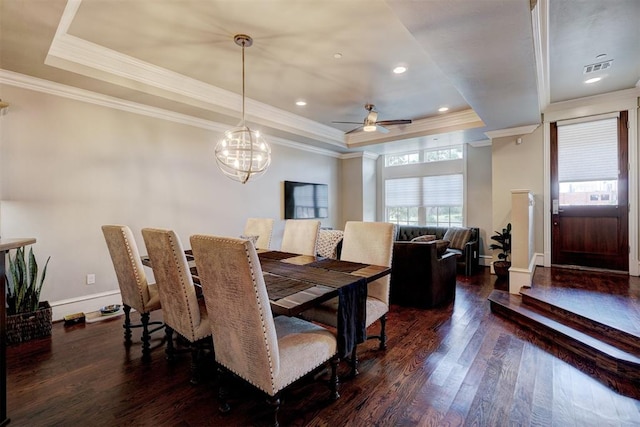 dining space with a tray ceiling, dark hardwood / wood-style flooring, ceiling fan with notable chandelier, and ornamental molding